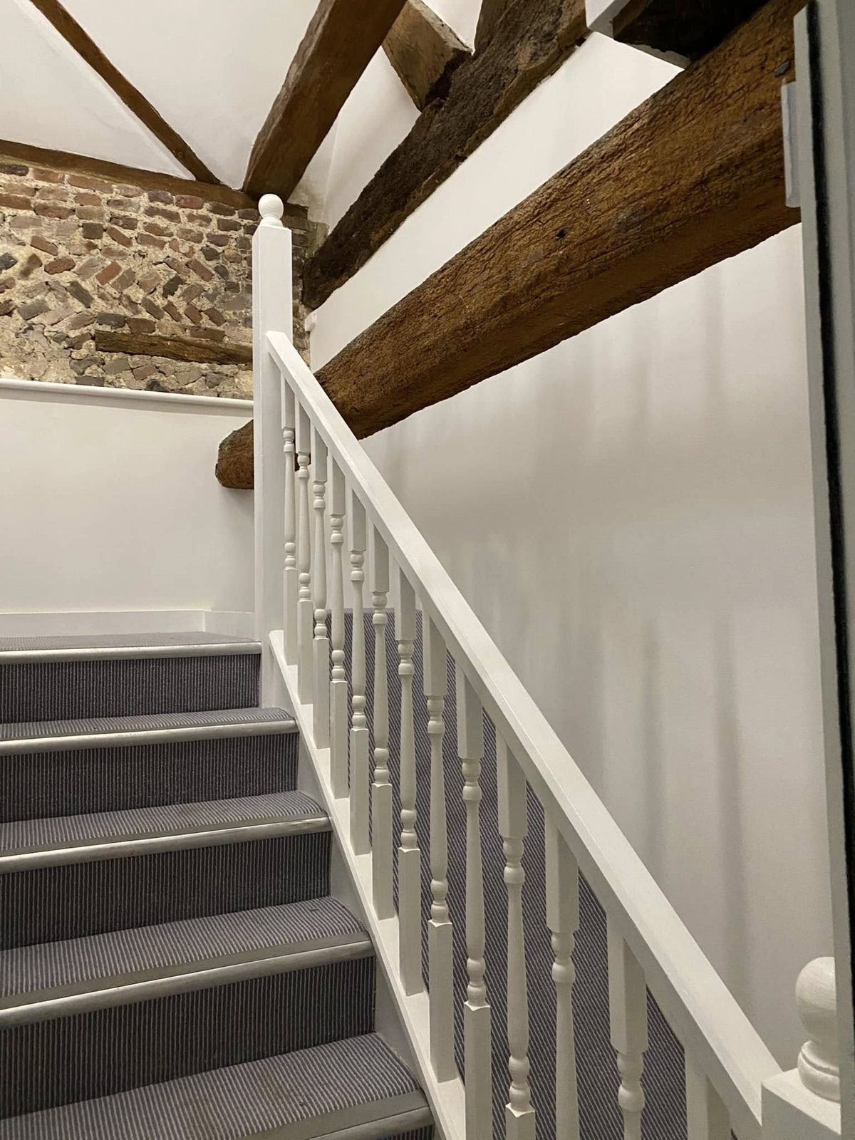 White staircase beneath massive oak beams beside exposed brick