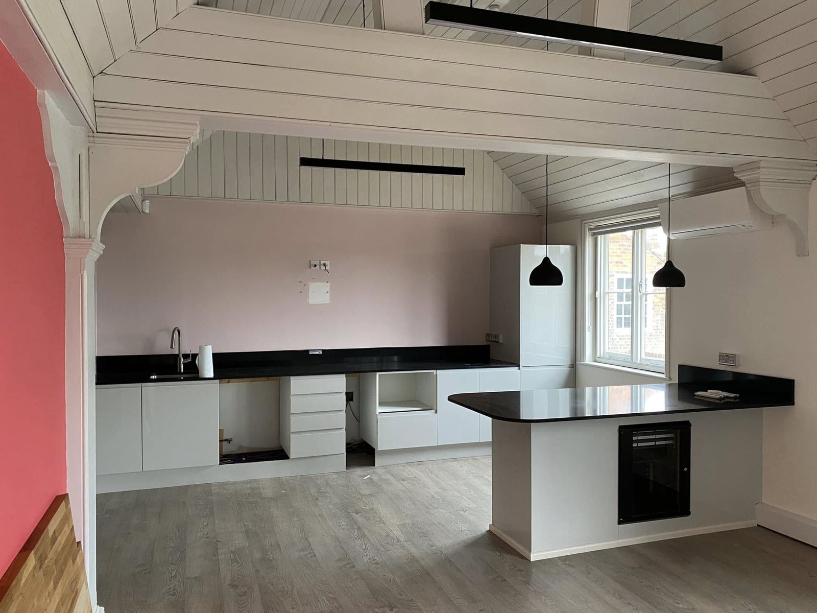 Kitchen run with black worktops beside a coral-red wall
