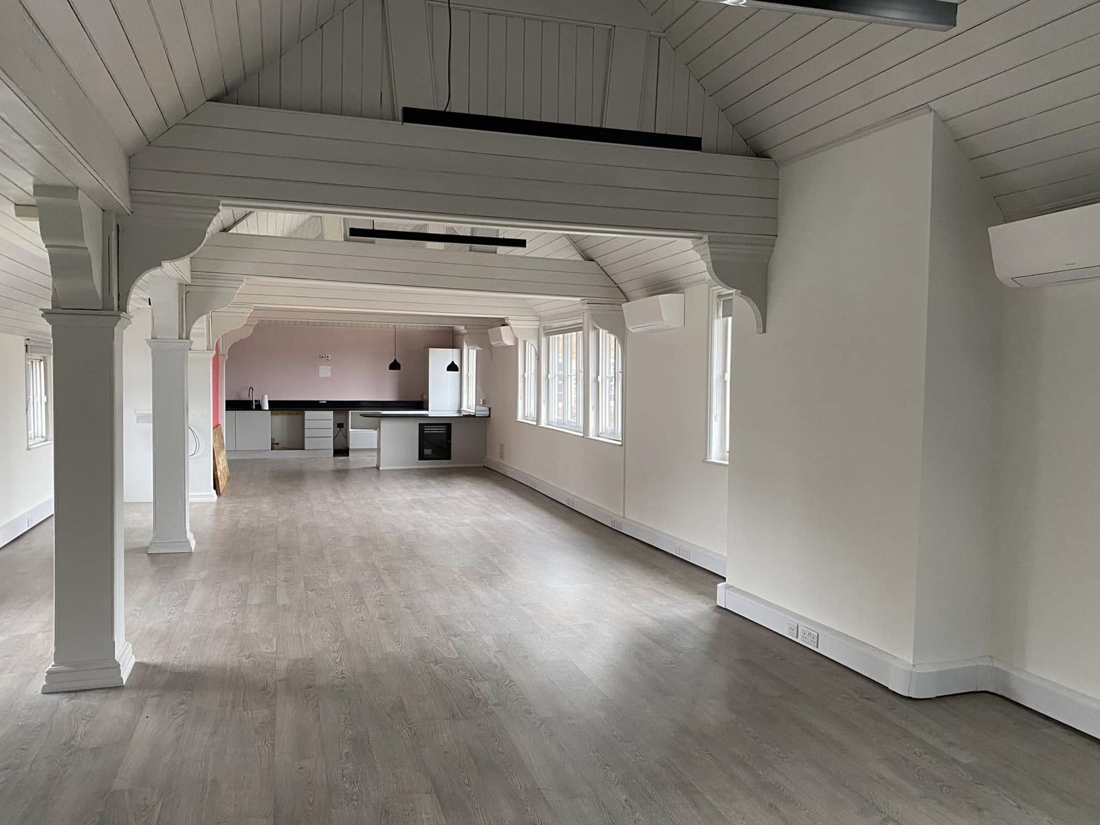Long open-plan room with columns and a white boarded ceiling