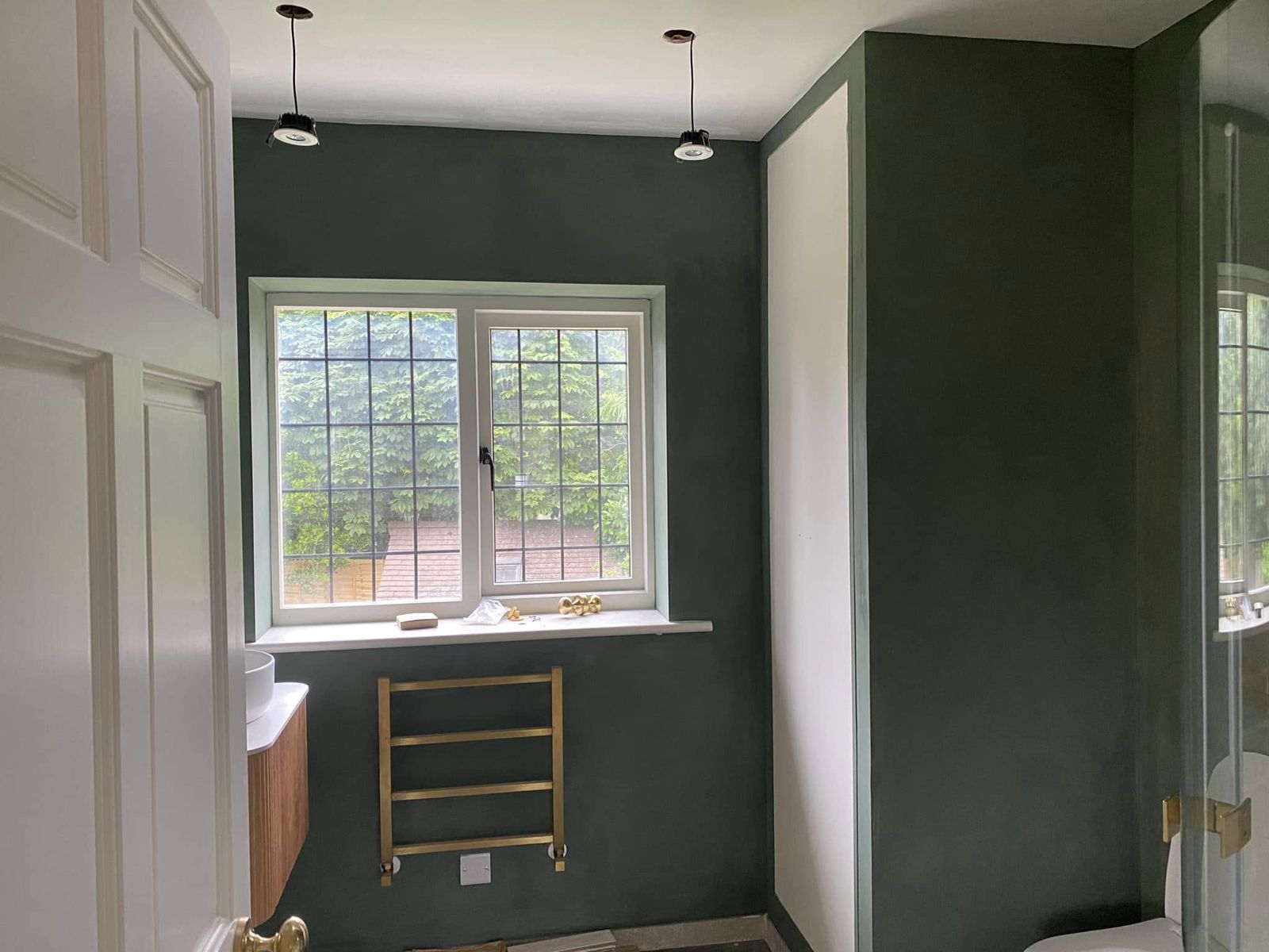 Bathroom with deep green walls, a brass towel rail and a leaded window