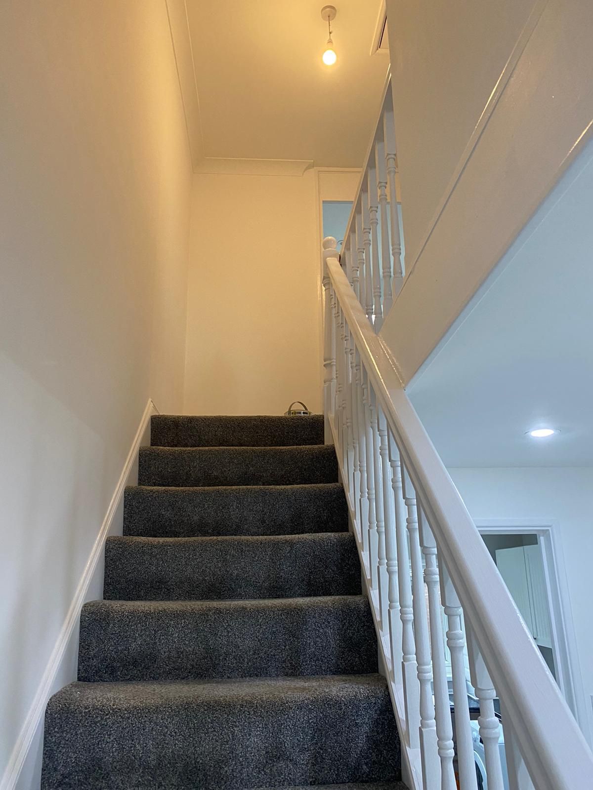 Narrow hall and staircase with white spindles and grey carpet